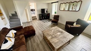 A living room with a sofa, armchairs, a coffee table, a TV, and a staircase leading to another level.
