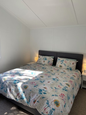 Un lit simple avec une couvre-lit à motifs floraux, deux lampes de chevet et une table de chevet.