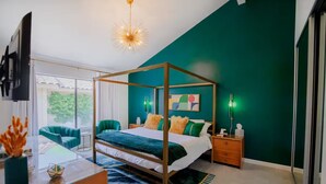 Un dormitorio con cama con dosel, televisor montado en la pared y un ventanal con vistas a la vegetación.