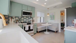 Una cocina moderna con microondas, estufa y armarios de colores claros. Hay una mesa redonda de comedor con mantel blanco y un sofá gris.