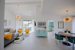 A modern living room with a sofa, yellow chairs, a dining table with chairs, a teal cabinet, and pendant lighting. - 2 Pools, Golf View, 2 Kings, 1 Full, 1 Twin, Luxury Home (Palm Desert)