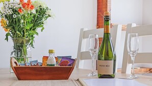 Een tafel met een fles wijn, twee glazen, een bloemenvaas en een houten doos met lekkernijen.