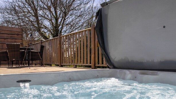 Un jacuzzi con terraza de madera, sillas y valla.