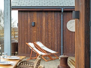 A wooden deck with two lounge chairs, a table with plates, and a decorative item on the wall. - Truffle House - UKC9375 (Westward Ho!)