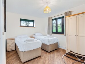 A bedroom with two beds, a wooden floor, a hanging light fixture, a window with curtains, and a wardrobe. - Truffle House - UKC9375 (Westward Ho!)