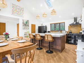 A modern kitchen with a central island, wooden chairs, a dining table, and pendant lighting. - Truffle House - UKC9375 (Westward Ho!)