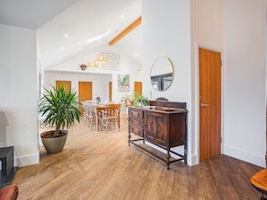 Una habitación amplia con suelo de madera, un comedor con mesa y sillas, una planta grande en maceta y un mueble de madera con cajones.