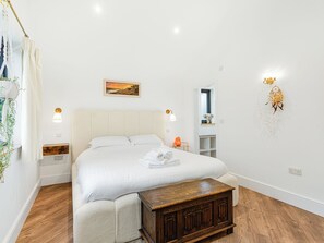 A neatly arranged bedroom with a bed, bedside tables, a nightstand, a wooden bench, a wall-mounted shelf, and a painting. - Truffle House - UKC9375 (Westward Ho!)