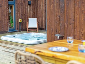 A wooden deck with a hot tub, a table with plates, and a chair. - Truffle House - UKC9375 (Westward Ho!)