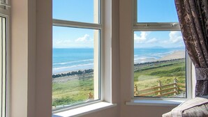 A room with two windows overlooking a beach and grassy landscape. - Bryn Eglwys - UKC9411 (Barmouth)