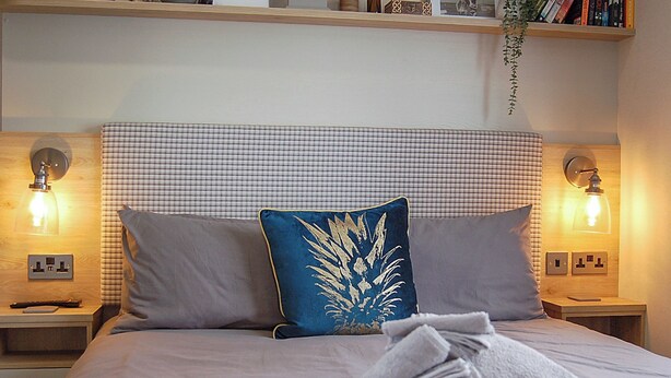 A neatly made bed with a checkered headboard, two bedside lamps, and a folded towel on the bed. - 2 bedroom accommodation in Tywyn (Tywyn)