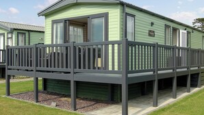 A green mobile home with a balcony and a fenced deck area. - 2 bedroom accommodation in Tywyn (Tywyn)