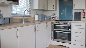 A kitchen with white cabinets, a stainless steel range hood, a built-in oven, a toaster, and a window with blinds. - 2 bedroom accommodation in Tywyn (Tywyn)