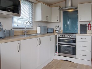 Eine Küche mit weißen Schränken, einer Edelstahl-Dunstesse, einem eingebauten Backofen, einem Toaster und einem Fenster mit Jalousien.