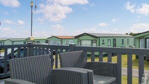 A patio area with wicker furniture, a railing, and a view of green mobile homes in the background. - 2 bedroom accommodation in Tywyn (Tywyn)