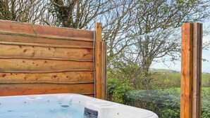 Un bain à remous entouré d’une clôture en bois, avec de la verdure en arrière-plan.