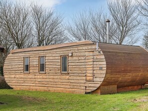 Eine Blockhütte mit gewölbter Dachform, zwei Fenstern und einem Schornstein.