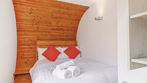 Une chambre à coucher avec une tête de lit en bois, du linge de lit blanc, deux oreillers rouges et une serviette blanche roulée posée sur le lit.