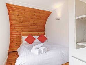 Ein Schlafzimmer mit hölzernem Kopfteil, weißer Bettwäsche, zwei roten Kissen und einem aufgerollten weißen Handtuch auf dem Bett.