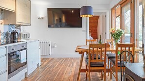 Une cuisine moderne dotée d’un four encastré, un coin repas avec des meubles en bois et une grande fenêtre offrant une vue dégagée.