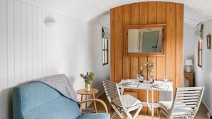 Et værelse med en blå sofa, et træspisebord dækket med tallerkener, glas og en flaske, samt et spejl over bordet.