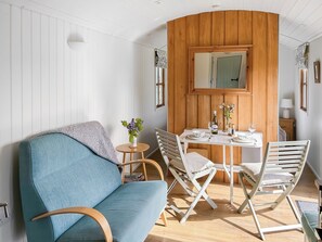 A room with a blue sofa, a wooden dining table set with plates, glasses, and a bottle, and a mirror above the table. - Looking for a romantic getaway. (St Buryan)