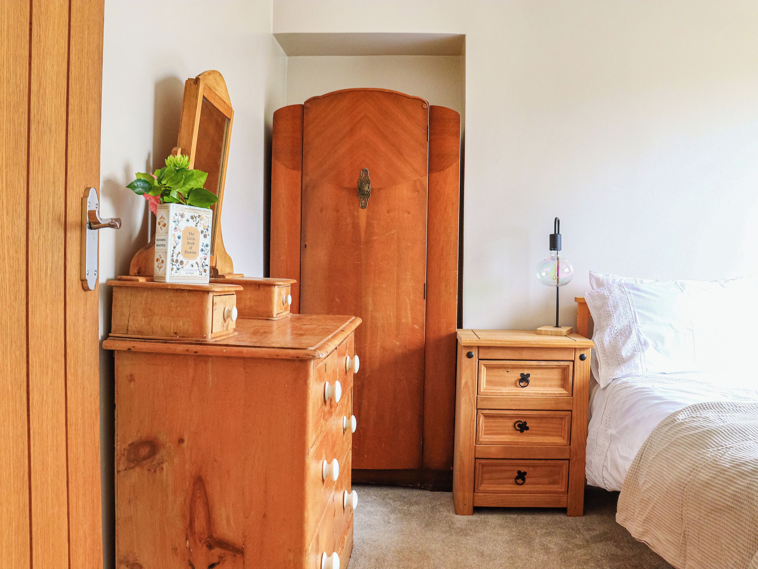 Een slaapkamer met een houten dressoir, een nachtkastje met een lamp en een bed.