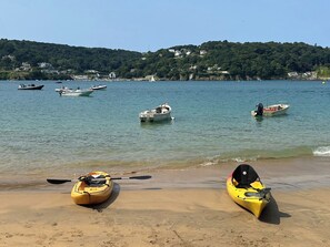 A beach with kayaks and boats on the water, a clear sky, and houses on a hill in the background. - 4 bedroom accommodation in Bovey Tracey (Bovey Tracey)