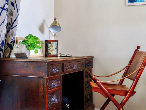 A wooden desk with drawers, a lamp, a framed picture, and a potted plant.