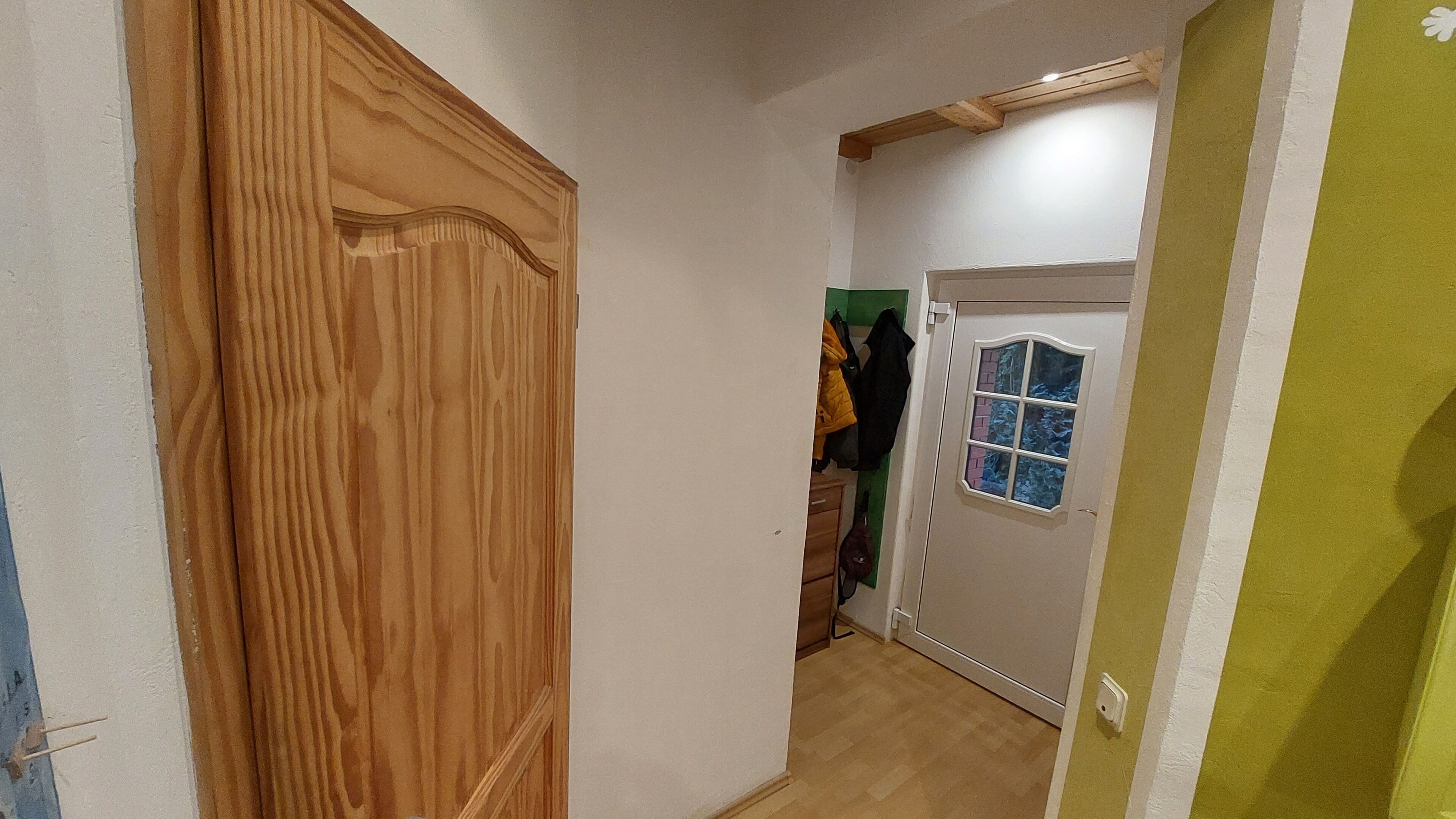Un pasillo con una puerta de madera, una puerta blanca con ventanal y una pared verde.