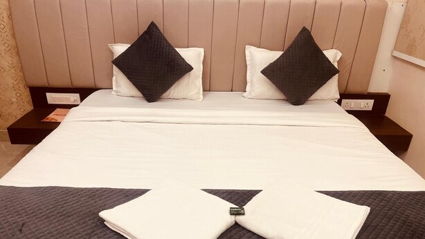A neatly made bed with a folded white towel in the center, two pillows, and a headboard. - Maa Prabha Courtyard (Varanasi)