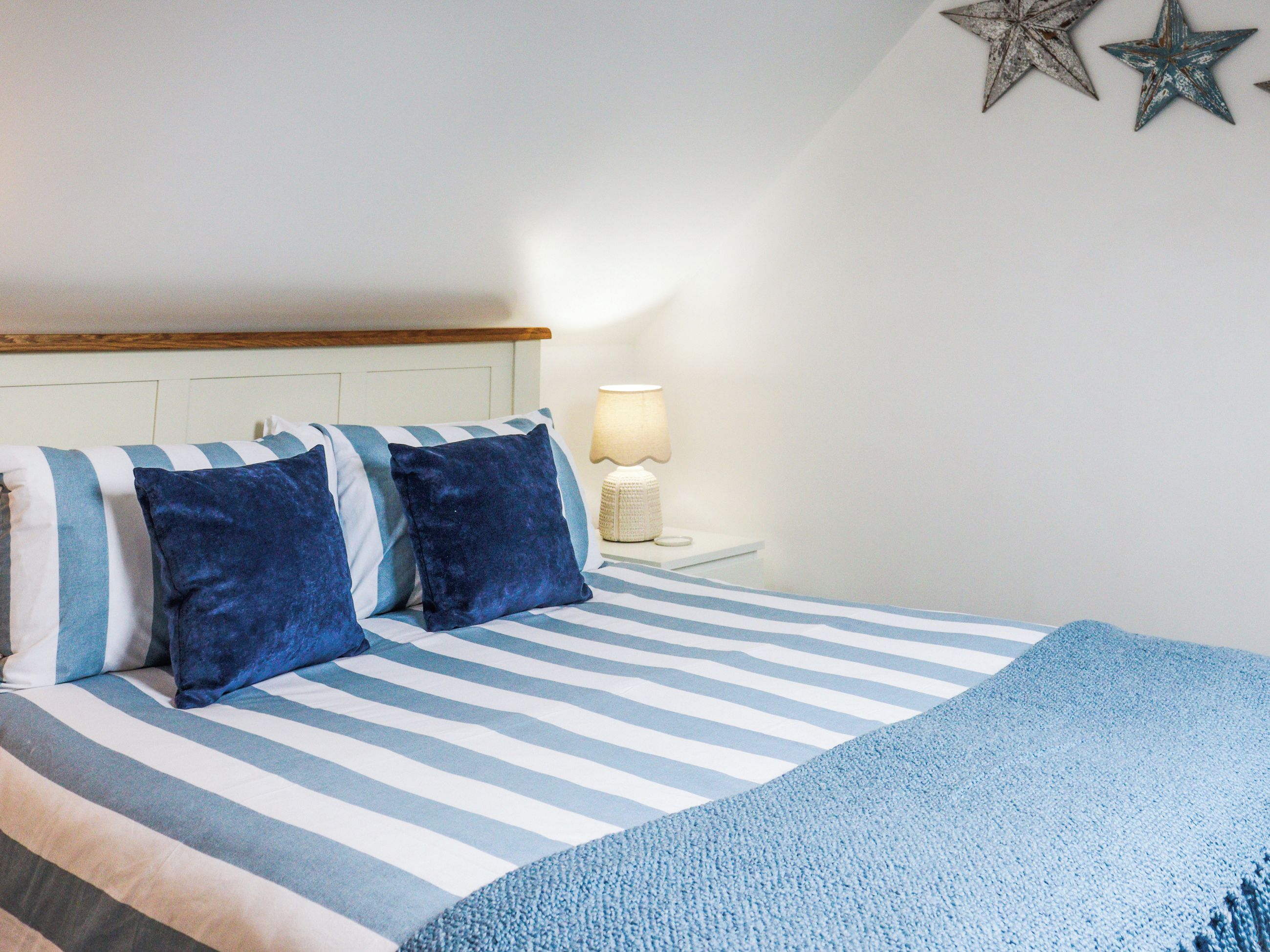 Un lit avec une literie à rayures, une lampe de chevet et des étoiles décoratives sur le mur.