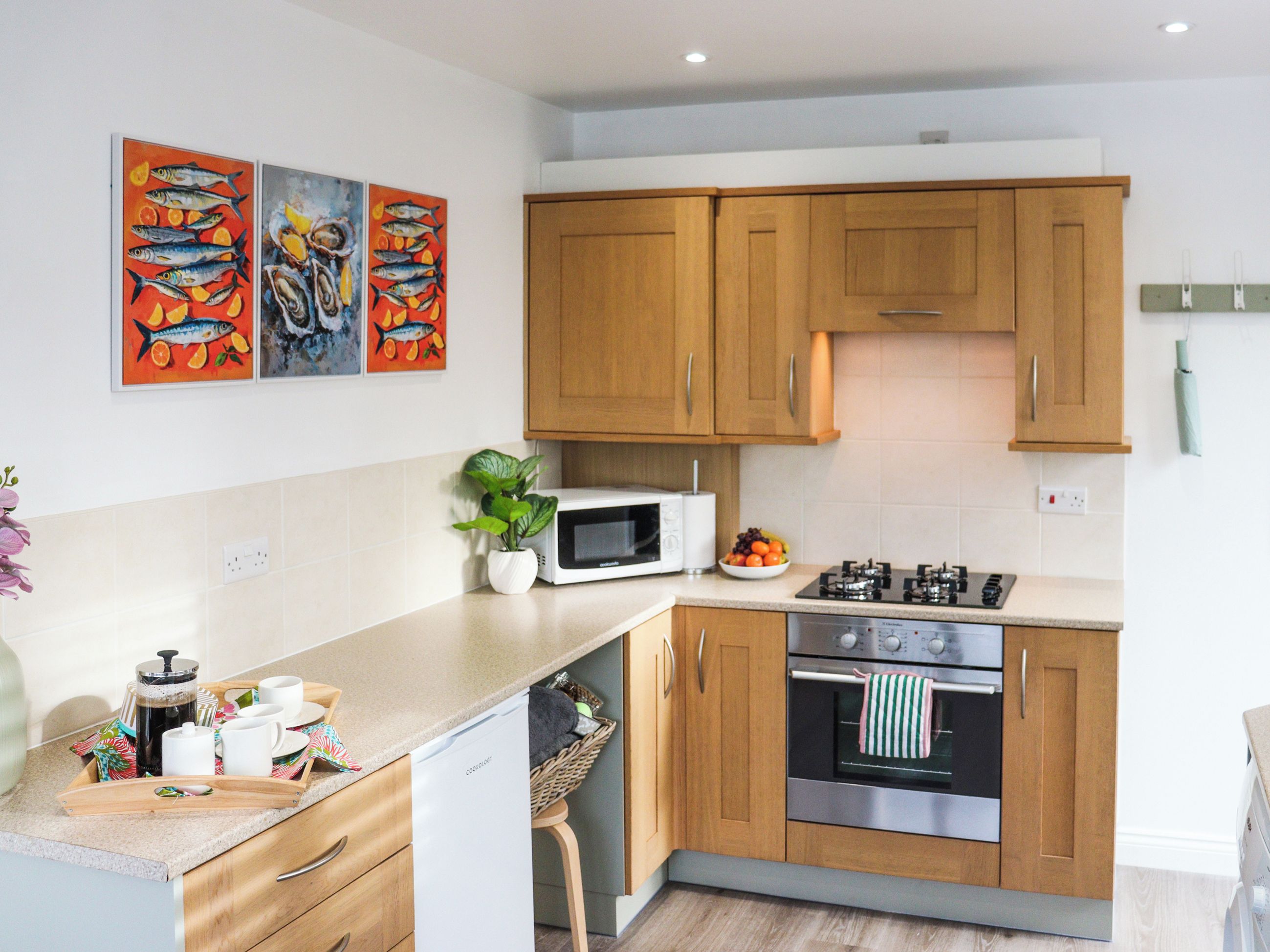 A modern kitchen with wooden cabinets, a microwave, a stove, and a dishwasher. There are three colorful fish paintings on the wall.