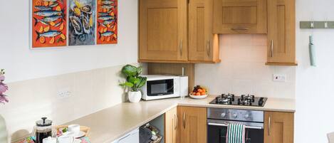 A modern kitchen with wooden cabinets, a microwave, a stove, and a dishwasher. There are three colorful fish paintings on the wall.