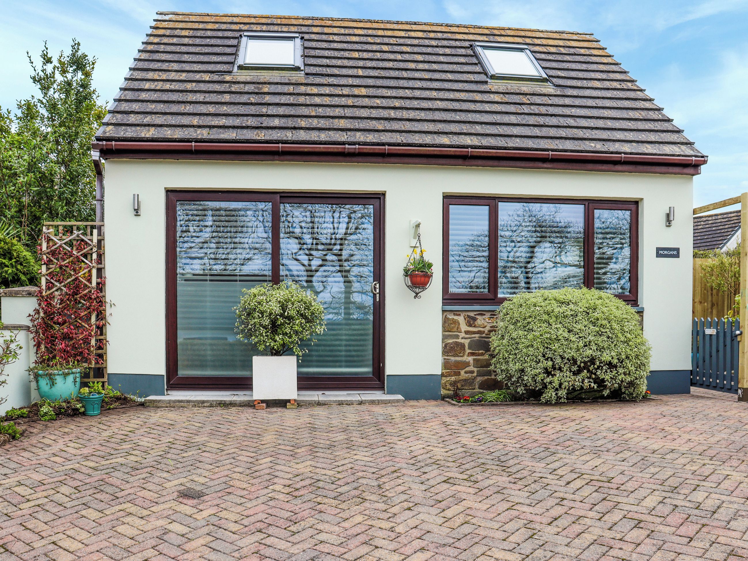A two-story house with a tiled roof, a front door, and a small garden area with potted plants and a hedge.