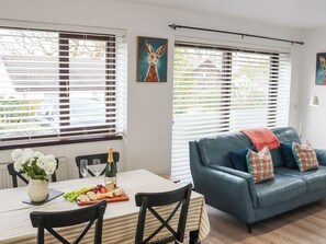 A dining area with a table set for two, a blue sofa with patterned cushions, and a window with blinds. - 1 bedroom accommodation in Narberth (Narberth)