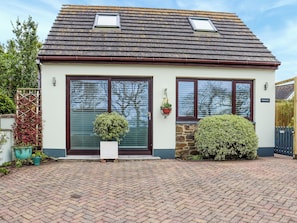 Ein zweistöckiges Haus mit Ziegeldach, einer Haustür und einem kleinen Garten mit Blumentöpfen und einer Hecke.