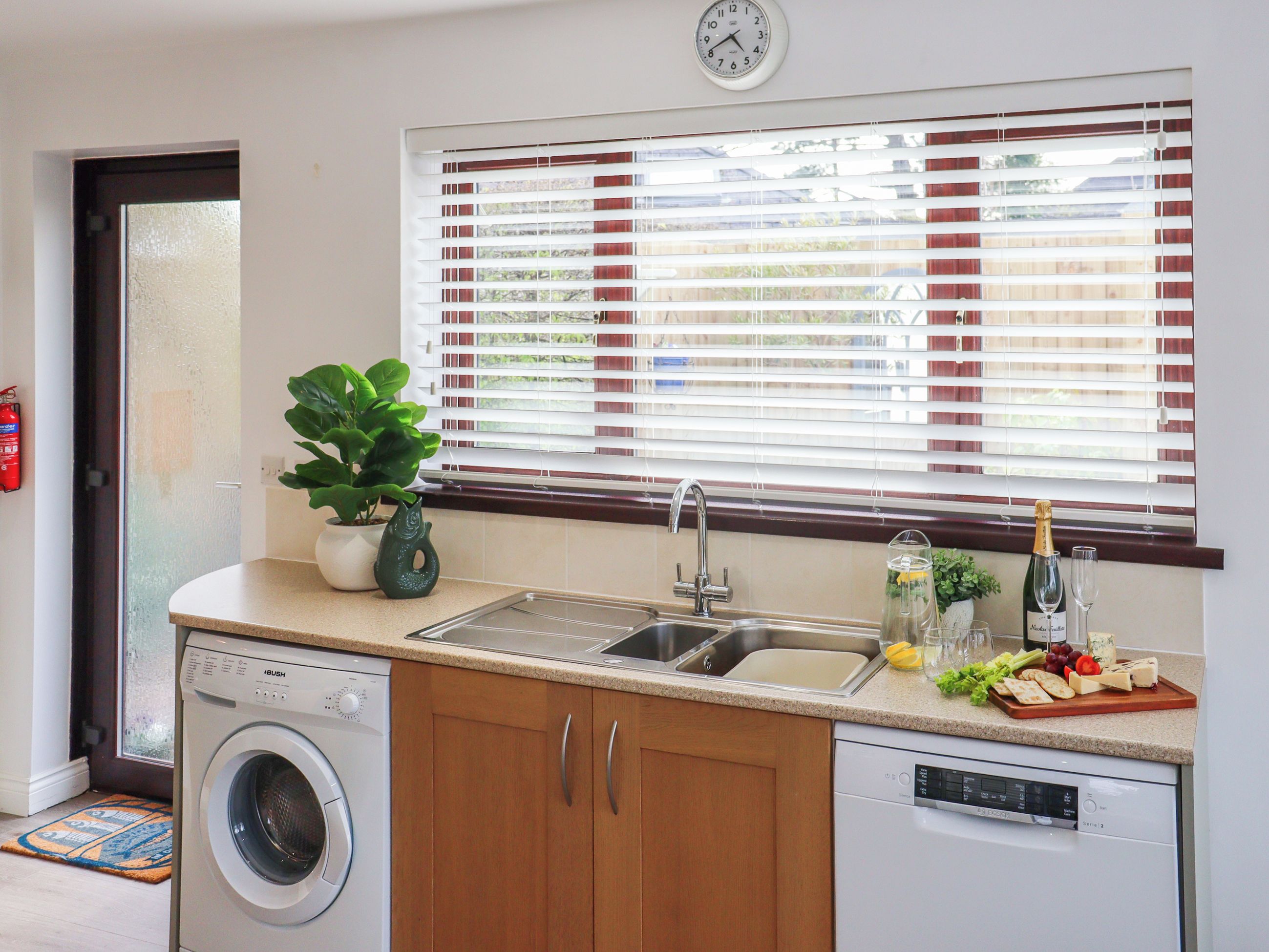 A kitchen with a washing machine, dishwasher, and a window with blinds.