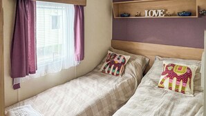 Een tweepersoonskamer met twee bedden, een raam met paarse gordijnen, een plankje met decoratieve objecten, en een wandplank met de tekst 'LOVE'.