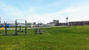 Een gazon met fitnessapparatuur, een houten omheining en stacaravans op de achtergrond.