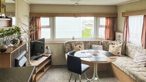 Een compacte leefruimte met een bank, een eettafeltje, een televisie en een kitchenette.