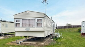 Een stacaravan met een schotelantenne, een klein terras en een gazon.