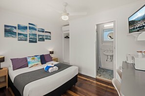 Ein Schlafzimmer mit Bett, Deckenventilator, Fernseher und einem Badezimmer mit Waschbecken und Spiegel.
