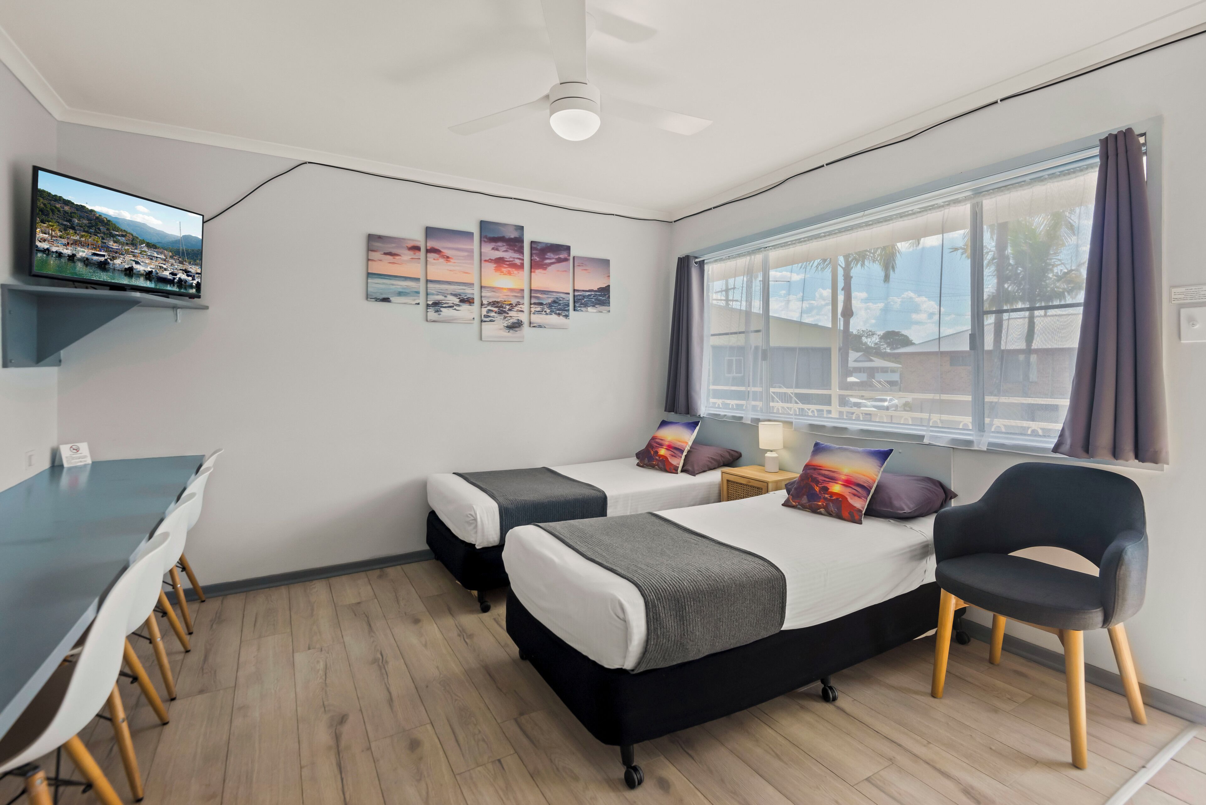 Een hotelkamer met een bed, nachtkastje, stoel, televisie, kunstwerk en een raam met uitzicht.