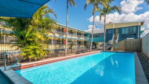 A swimming pool with a clear blue water, a wooden fence, and palm trees. - Pacific Motel Evans Head (Evans Head)