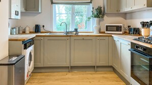 A compact kitchen with a washing machine, a microwave, and a stove. - Elm Tree House - UK51762 (Landford, near Salisbury)