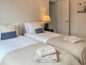 Habitació d'hotel amb dos llits, una tauleta de nit amb una làmpada, una porta i una paret amb una obra d'art.