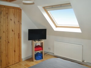 Ein Zimmer mit schrägem Dach, einem Oberlicht, einem Fernseher auf einem Holzboden, einer Heizung und einem Bett.