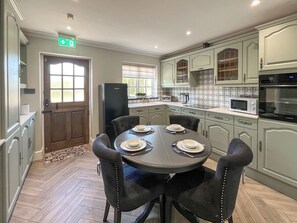 Una cocina con una mesa de comedor para cuatro personas, refrigerador, microondas y horno.