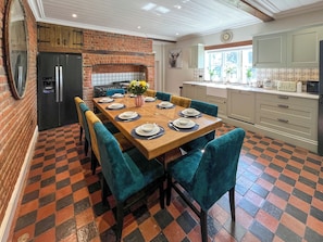 A dining area with a brick wall, a black refrigerator, a wooden table set for six, and teal chairs.